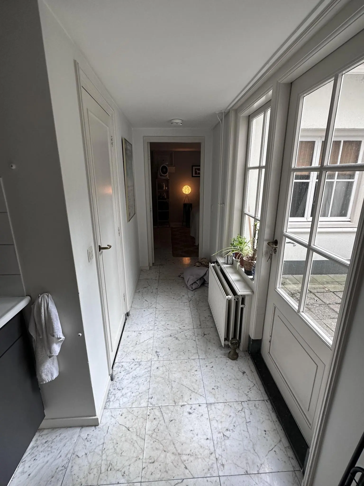 Smalle gang met marmeren vloer, wit geschilderde deuren en een doorkijk naar een verlichte kamer in een woning aan de Eerste Lindendwarsstraat.